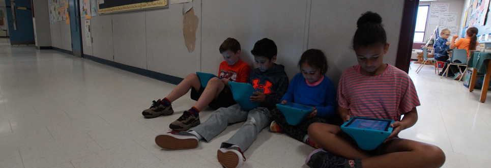 Male and female students using iPads in a hallway